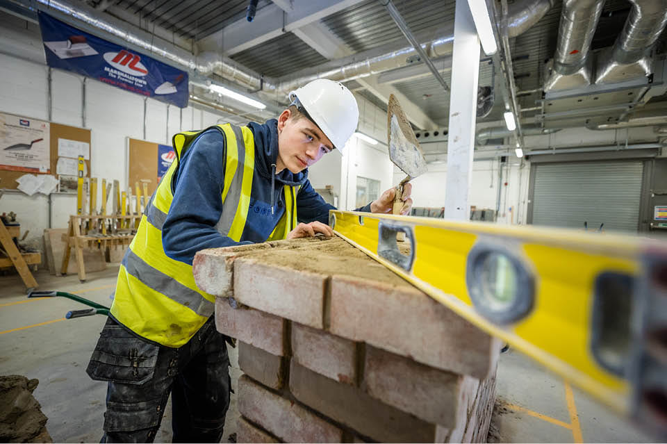 Apprentice bricklaying student using a spirit level on top of bricks