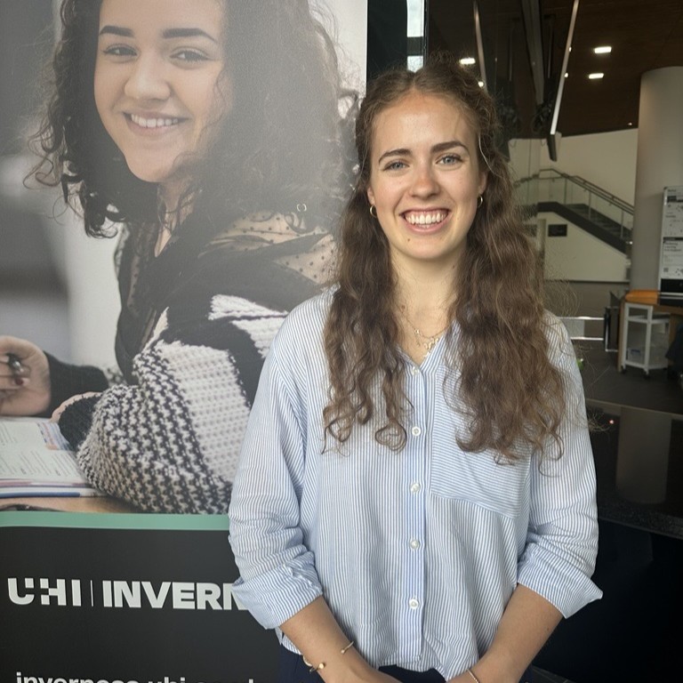student Amy Mustarde standing by college banner