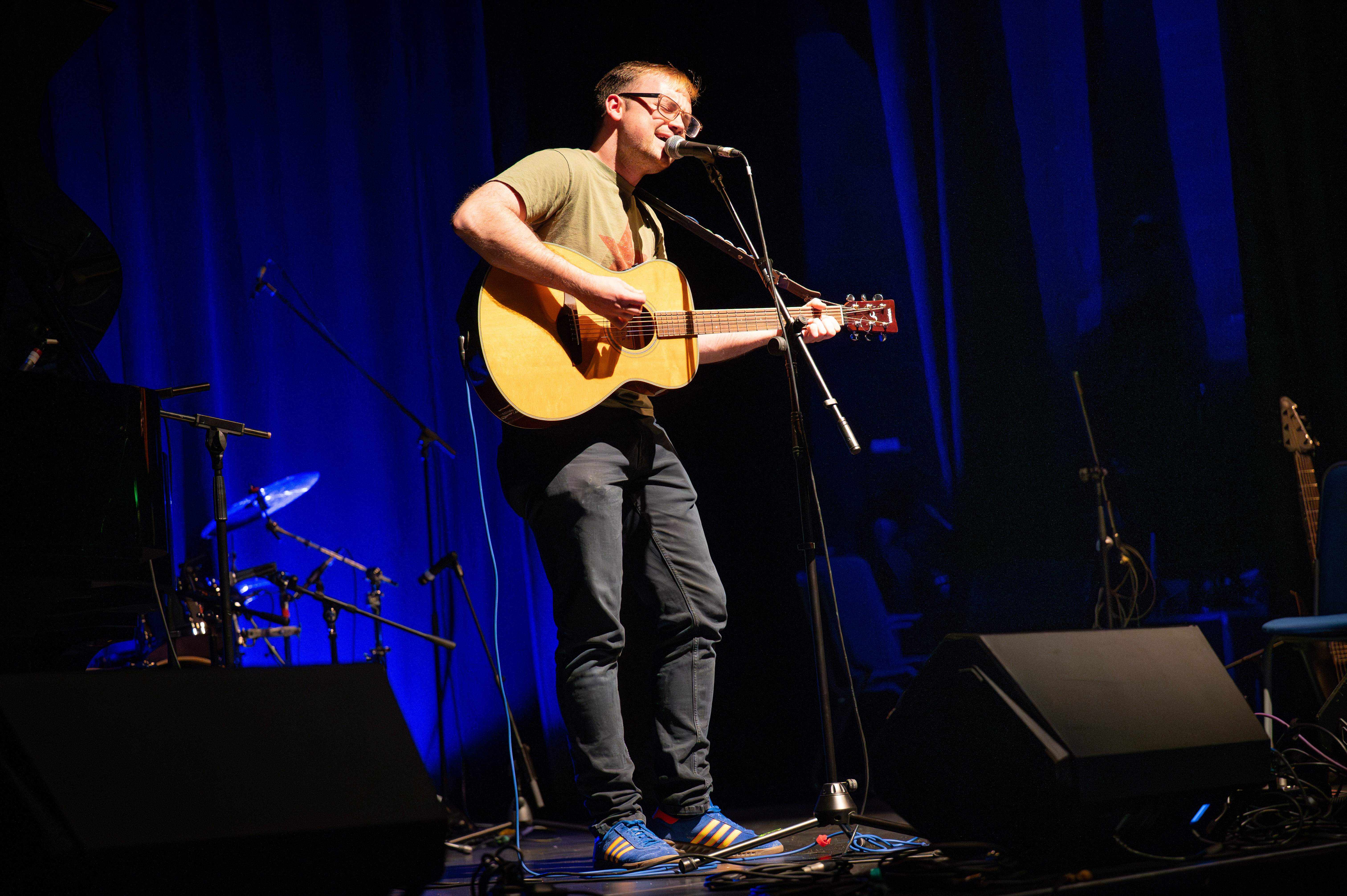 Music student on stage singing with guitar.