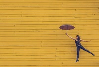 A person holding an umbrella in front of a yellow wall A person holding an umbrella in front of a yellow wall