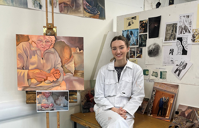 Fine art graduate Estella Smith in their studio with their artwork behind them