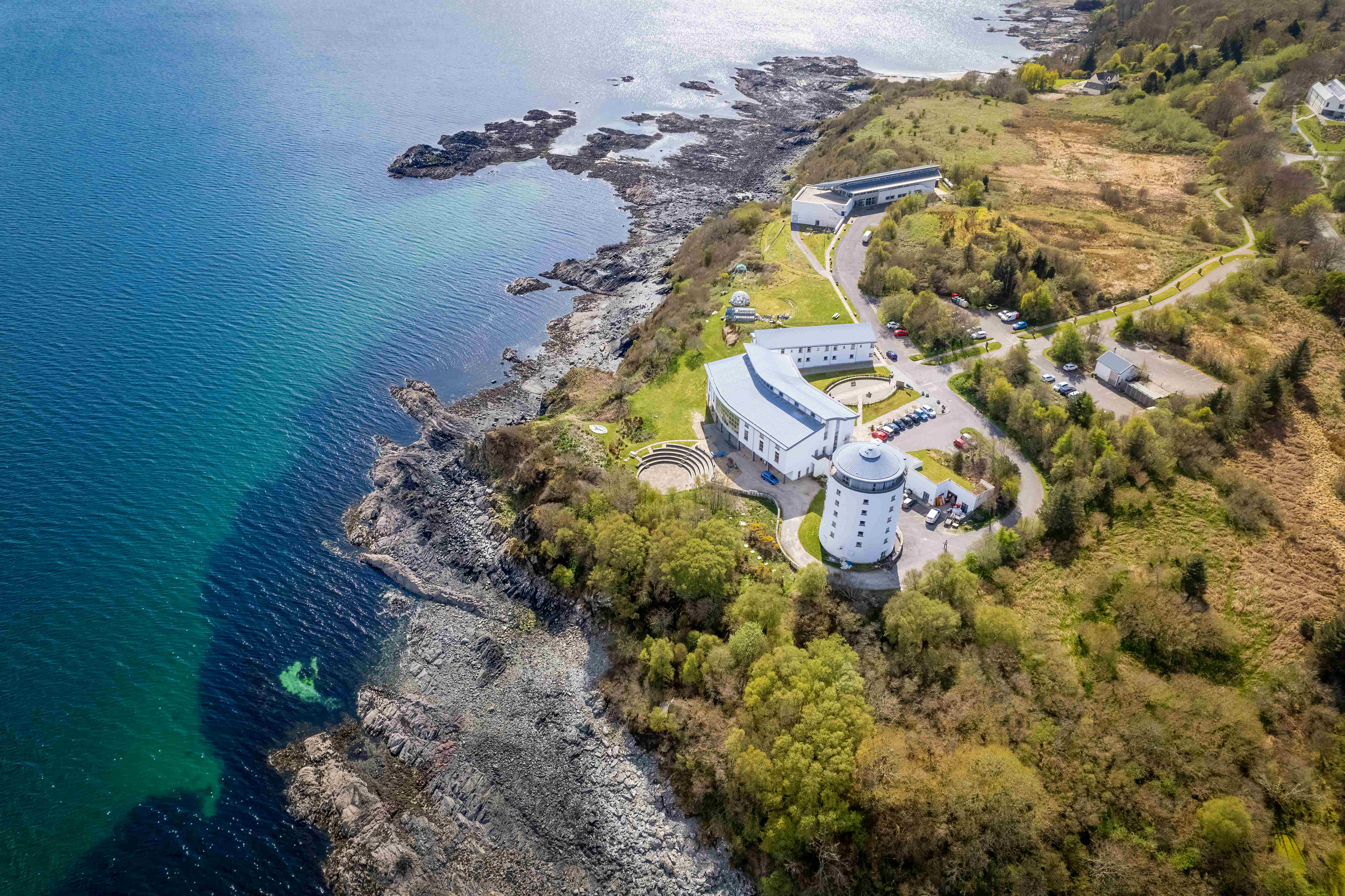 Aerial photo of a white building set by a rocky seashore, surrounded by greenery. Aerial photo of a white building set by a rocky seashore, surrounded by greenery.
