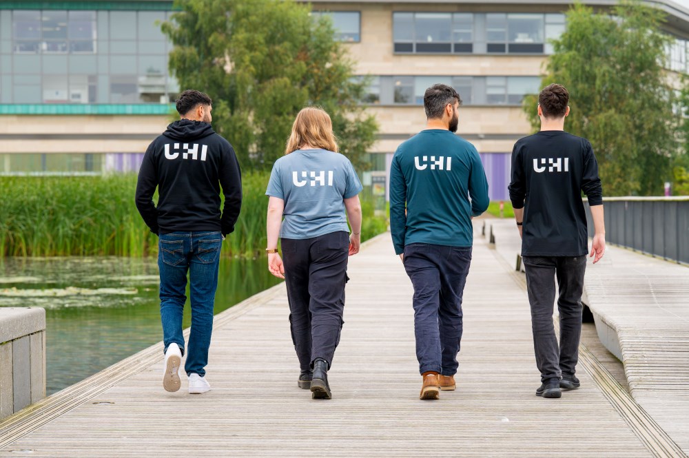 Four people walking away from the camera, each with UHI logo on their back Four people walking away from the camera, each with UHI logo on their back